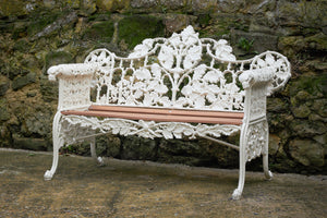a white floral iron bench with a slatted wooden seat